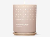 Et tændt beige lys mærket SKANDINAVISK ROSENHAVE Floral sanctuary står på en bordskåner af træ med et mønster af små hvide symboler på beholderen.
