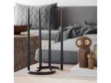 En moderne sort lysestage med fire høje stearinlys står på et bord ved siden af to uglefigurer i træ og en bog; en sofa og en træskammel står i baggrunden.