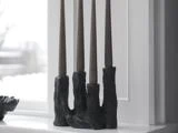 En sort, skulpturel lysestage med fire høje, mørke fyrfadslys står i en hvid vindueskarm foran et vindue.