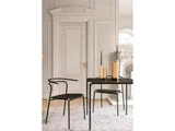 Et moderne sort bord med matchende stol står på et mønstret tæppe i et elegant rum med udsmykkede hvide paneler og en høj dør; der er gulddekoration og stearinlys på bordet.