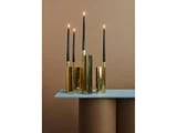 Fire tændte sorte bloklys i skinnende guldholdere står på et moderne lyseblåt bord mod en brun baggrund.