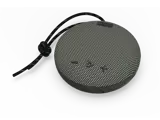 En rund, bærbar Bluetooth-højttaler med en struktureret overflade, tre kontrolknapper og en sort bærestrop på en lysegrå baggrund.