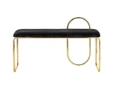 En moderne bænk med et sort, polstret sæde, guldfarvet metalstel og et unikt, cirkulært guldfarvet ryglæn på den ene side mod en hvid baggrund.
