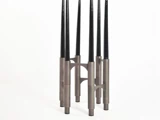 Et moderne skulpturelt objekt med fem lodrette sorte kegler understøttet af metalliske cylindriske baser og buede forbindelser på en hvid baggrund.