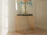 Et moderne sidebord med sort plade og guldtrådsfod står i et hjørne med en glasvase med pastelfarvede blomster og blade.