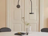 Minimalistisk spiseplads med et hvidt bord, sorte stole, moderne sorte pendler, glasvaser, en bakke og dobbelte cremefarvede paneldøre i baggrunden.