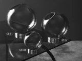 Tre glaskugler i forskellige størrelser, hver med en cirkulær åbning, er udstillet på en reflekterende sort overflade. Kuglerne er mærket Ø21, Ø17 og Ø10, hvilket angiver deres diameter.