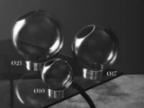 Tre klare glaskugler i forskellige størrelser med vinklede åbninger og metalbunde er udstillet på en glasoverflade. Kuglerne er mærket Ø21, Ø10 og Ø17, hvilket angiver deres diameter.