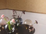 Flere runde glasvaser, nogle med lyserøde blomster og andre tomme, står på et mørkt bord mod en beige og hvid væg.