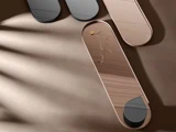 Rektangulær, rosafarvet bakke med afrundede ender holder en delikat guldhalskæde. To sorte bakker med samme form står ved siden af på en beige overflade med diagonale skygger.