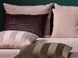 Fire pyntepuder i rosa, brune og beige nuancer er anbragt på en seng med en grøn væg i baggrunden.