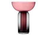 En moderne dekorativ glasvase med en bred, lav lyserød skål oven på en høj, cylindrisk mørkegrå base på en hvid baggrund.