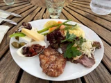 En hvid tallerken med grillet kød, ost, grøntsager, oliven, druer, gulerødder, asparges, kartoffelmos og tørrede tranebær på et træbord.