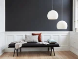 Et minimalistisk rum med en sort bænk, forskellige puder, et åbent magasin, to hvide pendellamper og vægge beklædt med mørkegrå og hvide paneler.