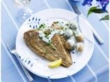 En tallerken med pandestegt fiskefilet, små kogte kartofler med hvid sauce, hakkede krydderurter og en citronbåd, dækket på en blåstribet dug.