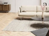 Moderne stue med beige sofa, gråt tæppe, rundt sort sofabord og en skænk i lyst træ i et minimalistisk, veloplyst rum.