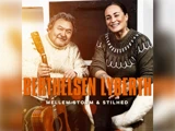 En ældre mand med en guitar og en smilende kvinde sidder sammen, begge iført strikkede trøjer. Tekst: BERTHELSEN LYBERTH og MELLEM STORM & STILHED.