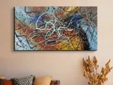 Abstrakt maleri med hvirvlende linjer og sprøjt i blå, sort og hvid på en baggrund af orange, gul og grå, der hænger på en beige væg over en sofa med puder og tørrede planter.