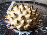 En dessert med spidse, ristede marengs på en mørk tallerken med kunstneriske stænk af hvide og lilla saucer.