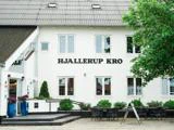 Hvid bygning med HJALLERUP KRO-skilt, udeservering med borde og stole, potteplanter og et træ, der delvist dækker facaden.
