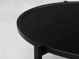 Nærbillede af et rundt, sort træbord med hævet kant på en lys, struktureret baggrund.