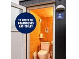Kig ind i et lille trætoilet med toilet og håndvask; på et skilt over døren står der 70 meter til bådhuse nat-toilet.