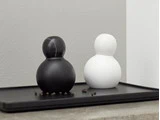 To runde, minimalistiske beholdere - en sort og en hvid - står på en rektangulær, sort bakke med et par peberkorn spredt i nærheden.