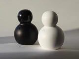To minimalistiske, runde figurer, der ligner bønder eller dukker, står side om side; den ene er sort, den anden hvid, på en almindelig, svagt oplyst flade.