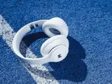Hvide over-ear-hovedtelefoner hviler på en struktureret blå overflade ved siden af en hvid linje, der kaster en skygge.