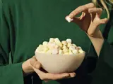 En person i grøn skjorte holder en skål med farverige mini marshmallows og samler en op med den anden hånd.