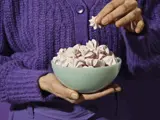 En person i en lilla sweater holder en skål med lyserøde og hvide marengskager og tager en op med hånden.