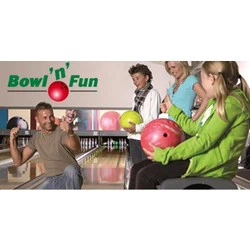 En gruppe på fire personer på en bowlingbane smiler og holder bowlingkugler; et Bowl n Fun-skilt ses i baggrunden.