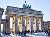 Brandenburger Tor i Berlin, Tyskland, med mennesker, der går og samles omkring søjlerne på en solrig dag.