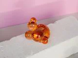 En lille, abstrakt orange glasskulptur med runde former sidder på en struktureret hvid mursten mod en pink baggrund.