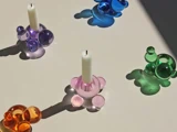 Fire farverige glaslysestager med bobleformer og hvide stearinlys kaster skygger på en lys overflade. Stagerne er orange, lilla, pink og grønne. En blå holder er tom.