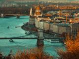 Luftfoto af Budapest med parlamentsbygningen, kædebroen og både på Donau-floden omgivet af efterårsløv.