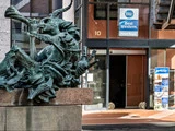 Bronzeskulptur af mytologiske væsner foran indgangen til Best Western Hotel Royal, hvor man kan se hotelskiltet og glasdørene.