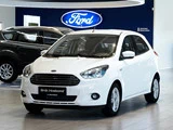 En hvid Ford hatchback er udstillet i et showroom med et stort blåt Ford-logo på væggen i baggrunden.