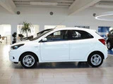 En hvid kompakt hatchback-bil er parkeret indendørs i et moderne showroom med flisegulv og stærk belysning.