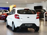 En hvid Ford Ka+ hatchback er udstillet indendørs i et biludstillingslokale, omgivet af andre biler under kraftig belysning.