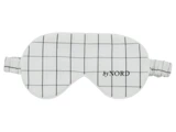 Hvid sovemaske med sort gittermønster og teksten by NORD trykt på højre side, med elastisk strop.