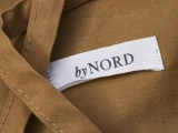 Et hvidt stofmærke med teksten byNORD er syet fast på et stykke brunt klæde.