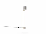 Stående lampe med et slankt, guldfarvet stativ, en cylindrisk grå lampeskærm og en sort strømledning.