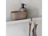 En beige sæbedispenser og en matchende beholder står på en hvid hylde med kroge under, der holder en brun strop og en netpose.