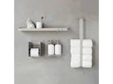 Minimalistisk vægopsætning på badeværelset med en hylde med tandbørsteholder og dekoration, en toiletpapirrulleholder, sæbedispensere og en strop med stablede toiletpapirruller.