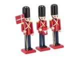 Tre legetøjssoldatfigurer i røde uniformer og høje sorte hatte; den ene holder et dansk flag, den anden en tromme og den sidste et gevær.
