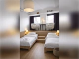 Et hotelværelse med to enkeltsenge på et lavere niveau og to lænestole på en forhøjet træplatform.