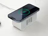 En smartphone oplades trådløst oven på en lille hvid rektangulær højttaler, der er placeret på en lys overflade.