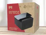 En æske med MIIEGO Charge&Play Re:duce Black Edition, en trådløs højttaler og ladestation, udstillet på en lys træoverflade.