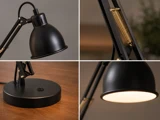 En collage bestående af fire nærbilleder af en sort, justerbar bordlampe, der viser lampeskærmen, fjedermekanismen, den runde fod med en knap samt lampen, når den er tændt.